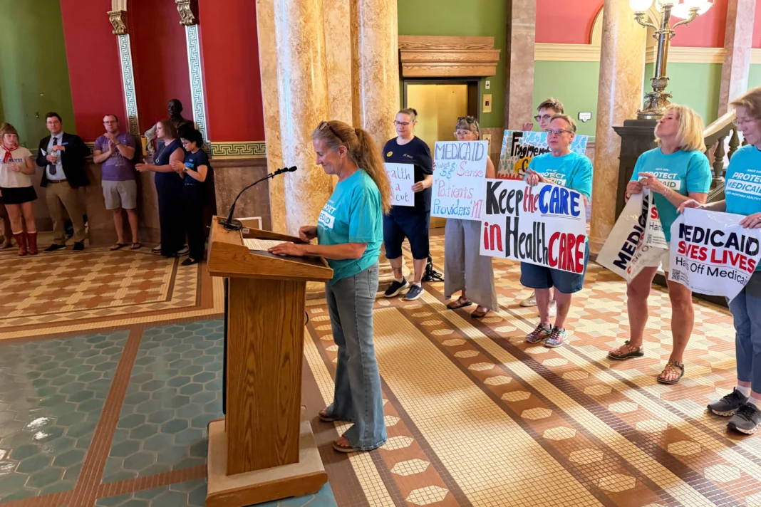 A photo of Rep. Mary Caferro speaking at a podium seen from a different angle. Behind her stand several women holding signs that read, 